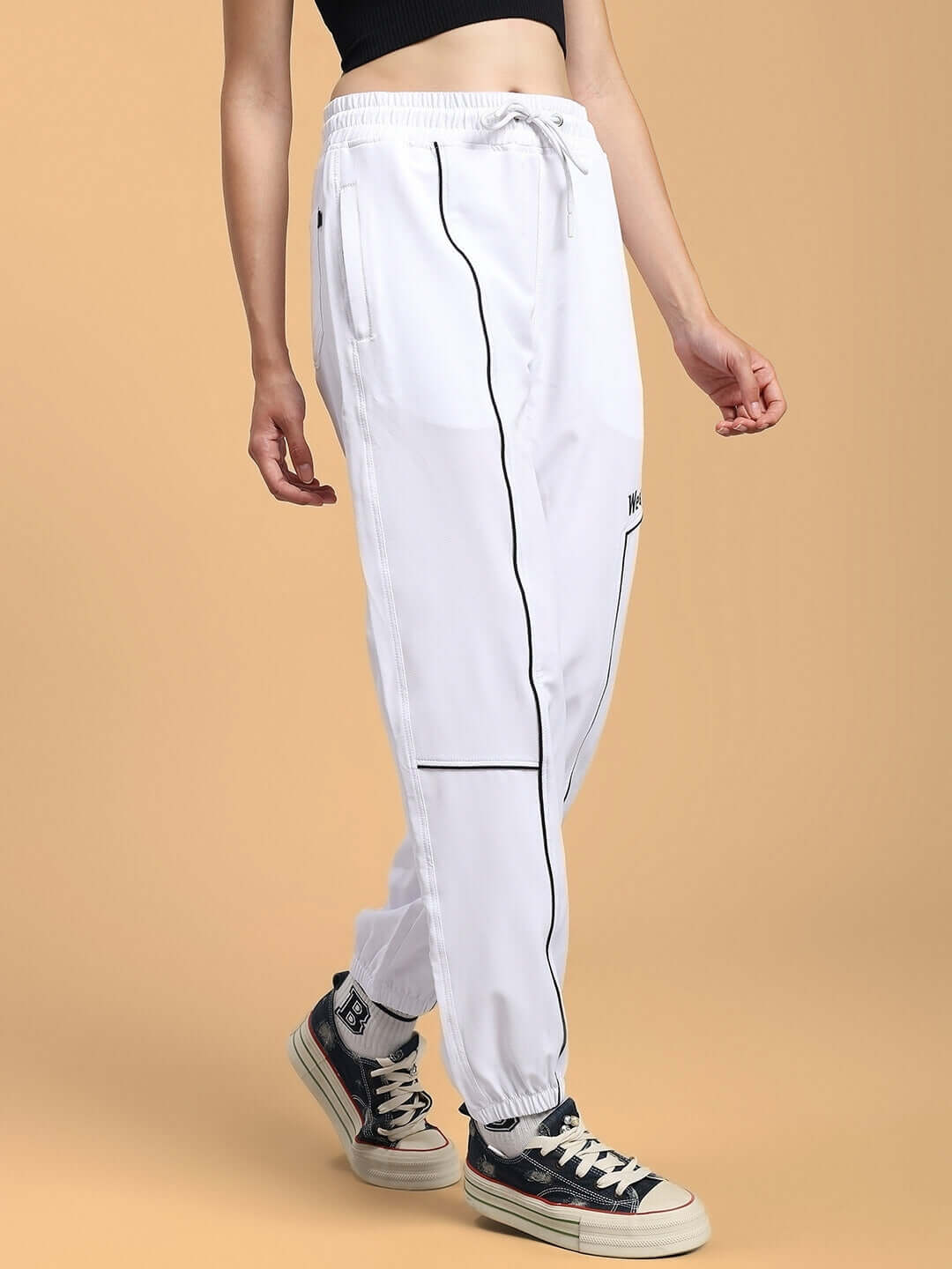 Women's white relaxed fit joggers with black piping, featuring a drawstring waist, displayed on a model with sneakers.