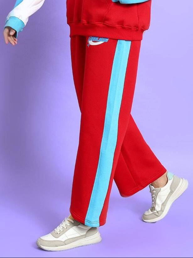 Women's red colorblock co-ord pants by DUDS with blue stripe, tailored fit, shown with white sneakers on a purple background.