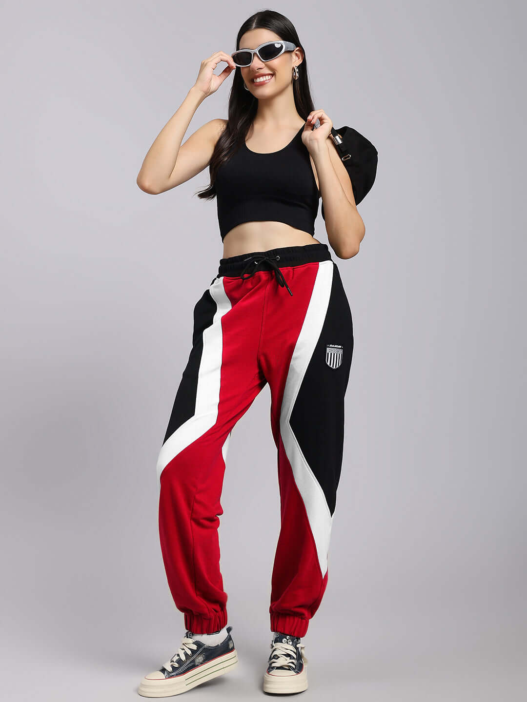 Woman wearing red and black colorblock joggers with a relaxed-fit, paired with a black tank top and sunglasses, showcasing urban style.