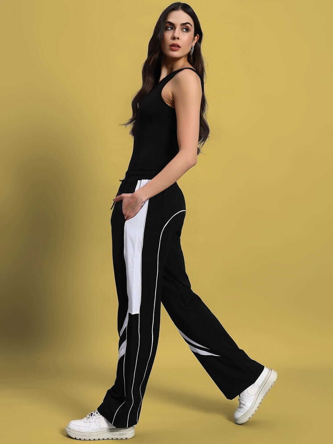 Woman wearing women's versatile parachute cargo pants in black with a custom fit option against a yellow background