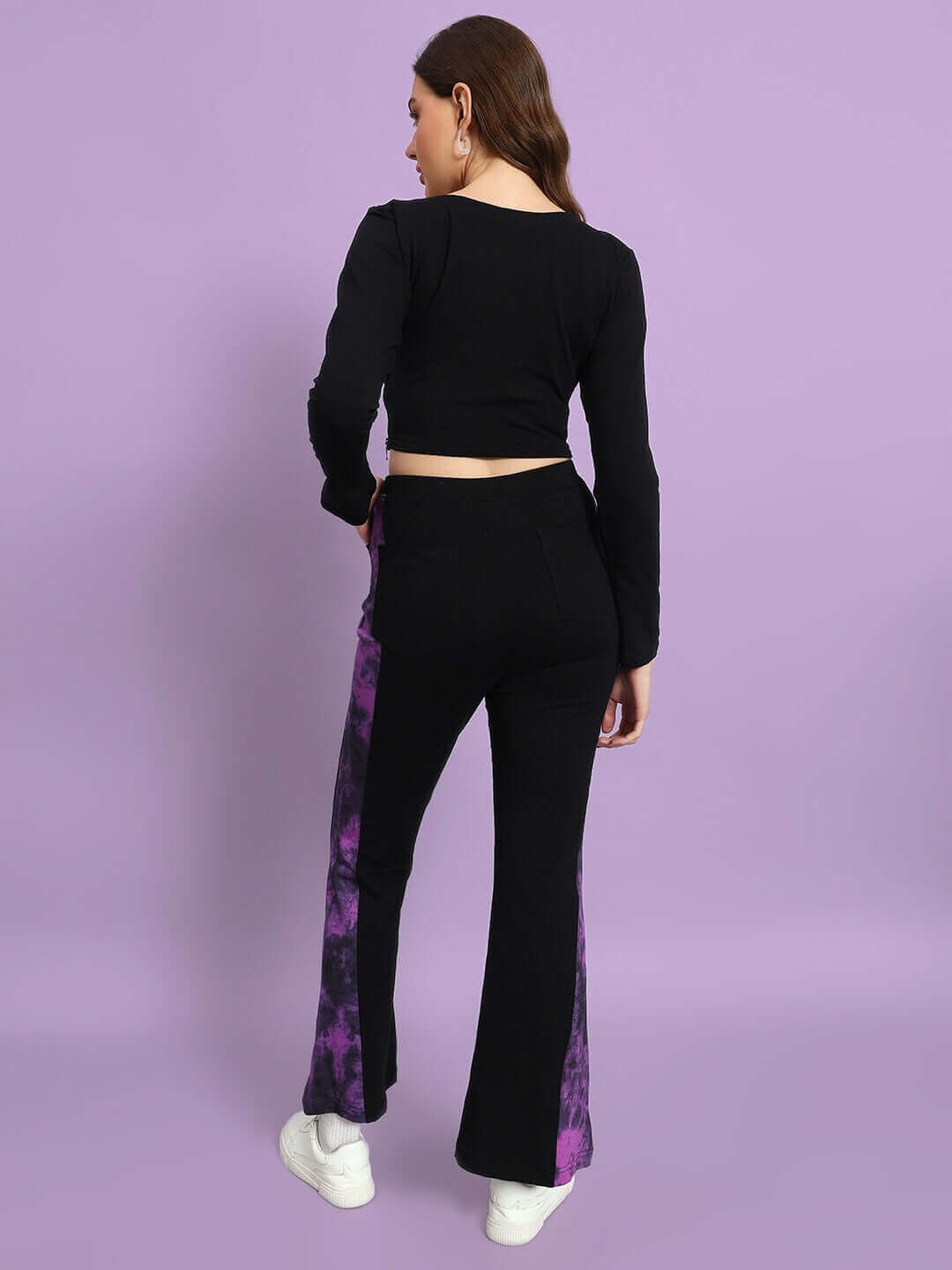 Back view of a woman wearing a black-purple tie-dye crop top and matching pants, standing against a purple background.