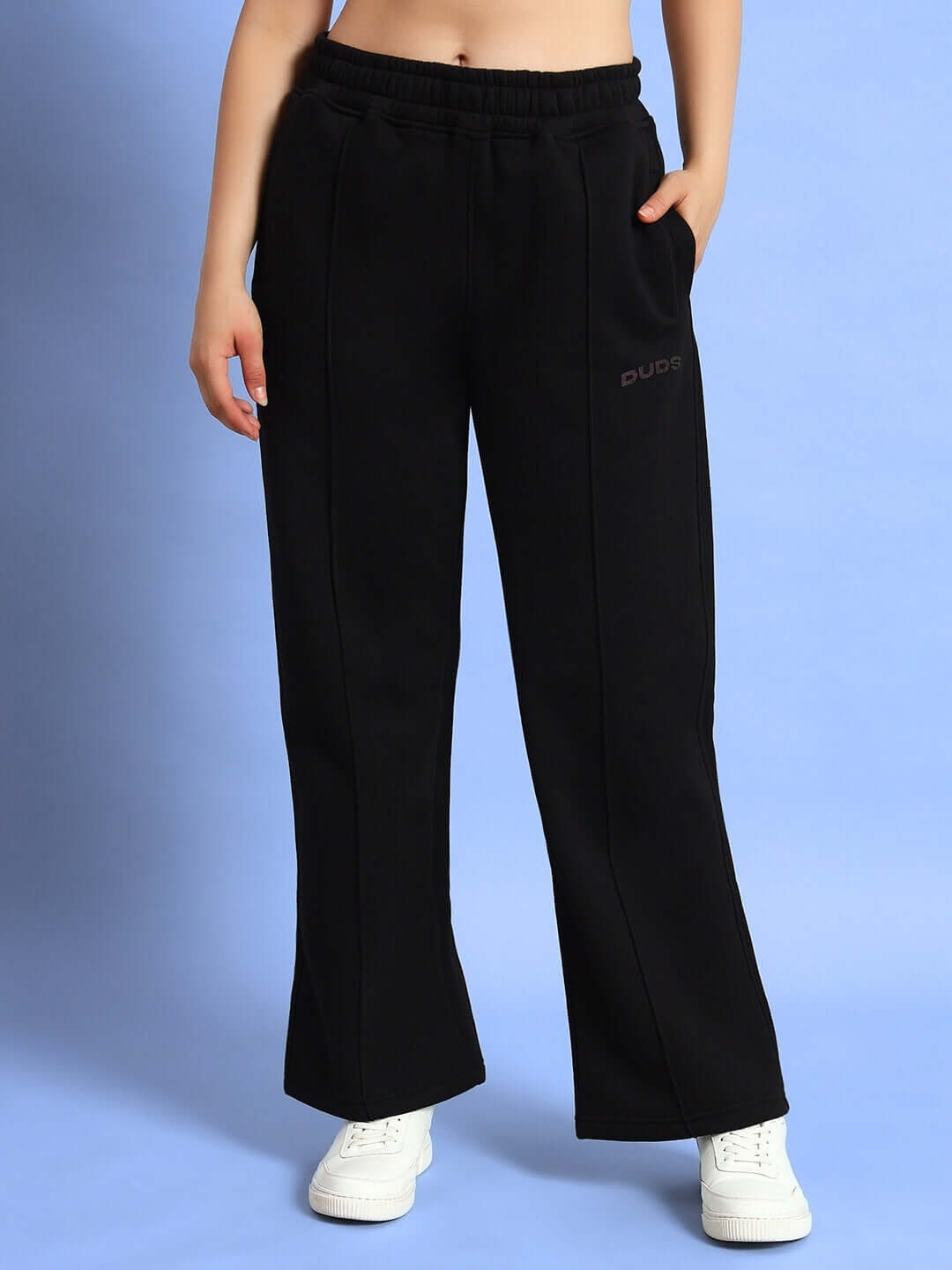 Model wearing WOMEN WD ADMIRE FLEECE CARGO PANT BLACK with white sneakers against blue background.