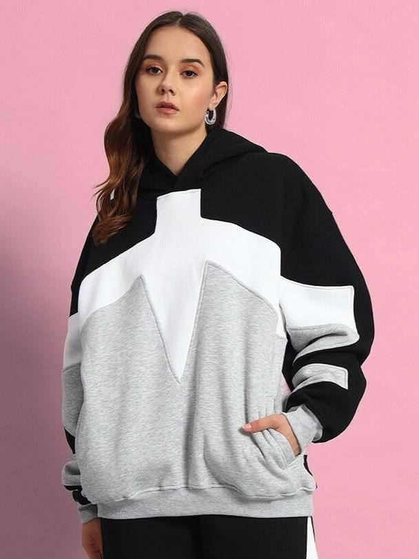 Model wearing WOMEN WD SWORD FLEECE COLORBLOCK HOODIE BLACK GREY with a pink background.