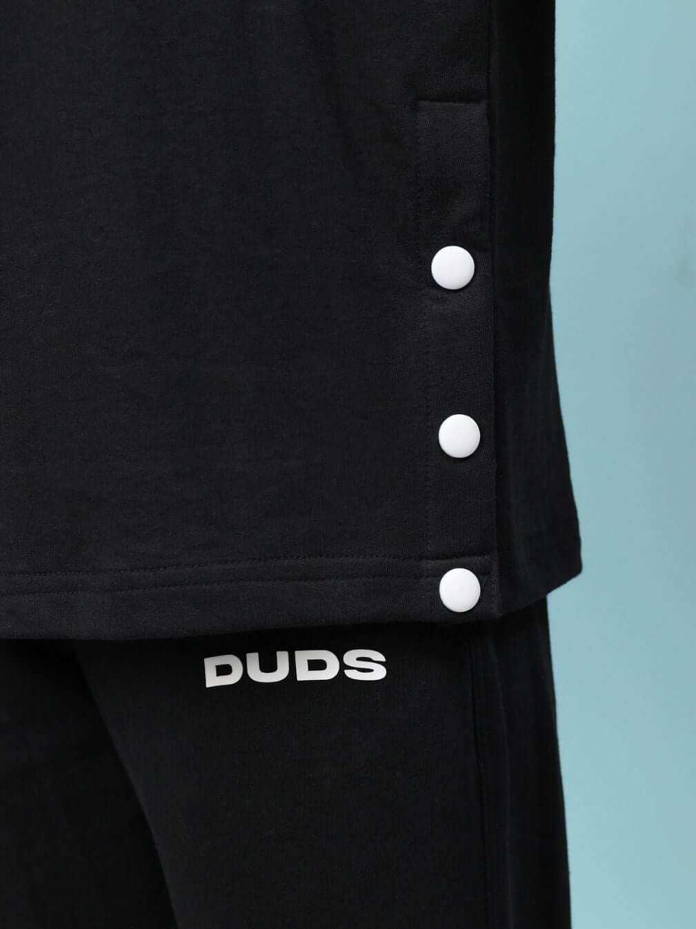 Close-up of black oversized women's T-shirt with button details, premium cotton fleece fabric, 240 GSM, and branding.