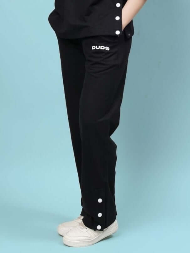 Model wearing black women's relaxed-fit jogger pants by DUDS, featuring side buttons, perfect for custom fit orders.