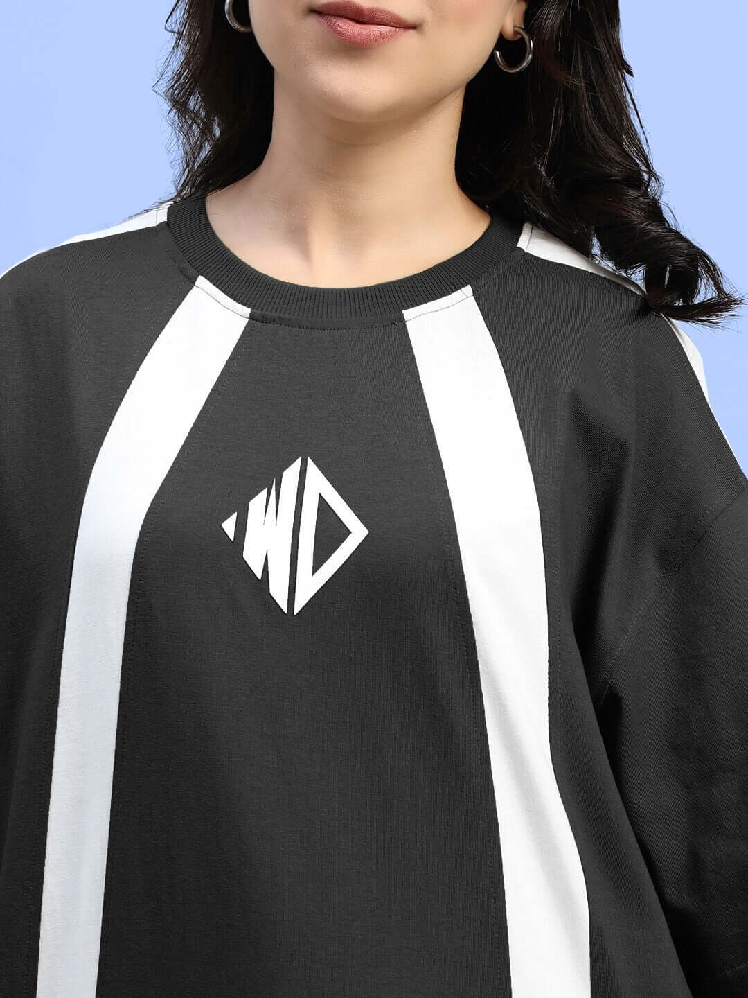 Woman wearing black oversized wideline T-shirt with white stripes, featuring premium cotton fabric and logo detail.