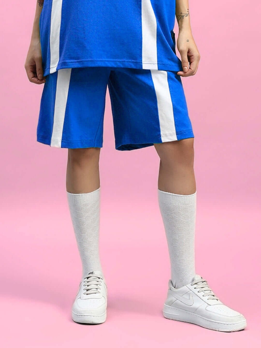 WOMENS WIDELINE REGULAR FIT SHORTS BLUE, styled with white sneakers and socks against a pink backdrop, showcasing the chic design.