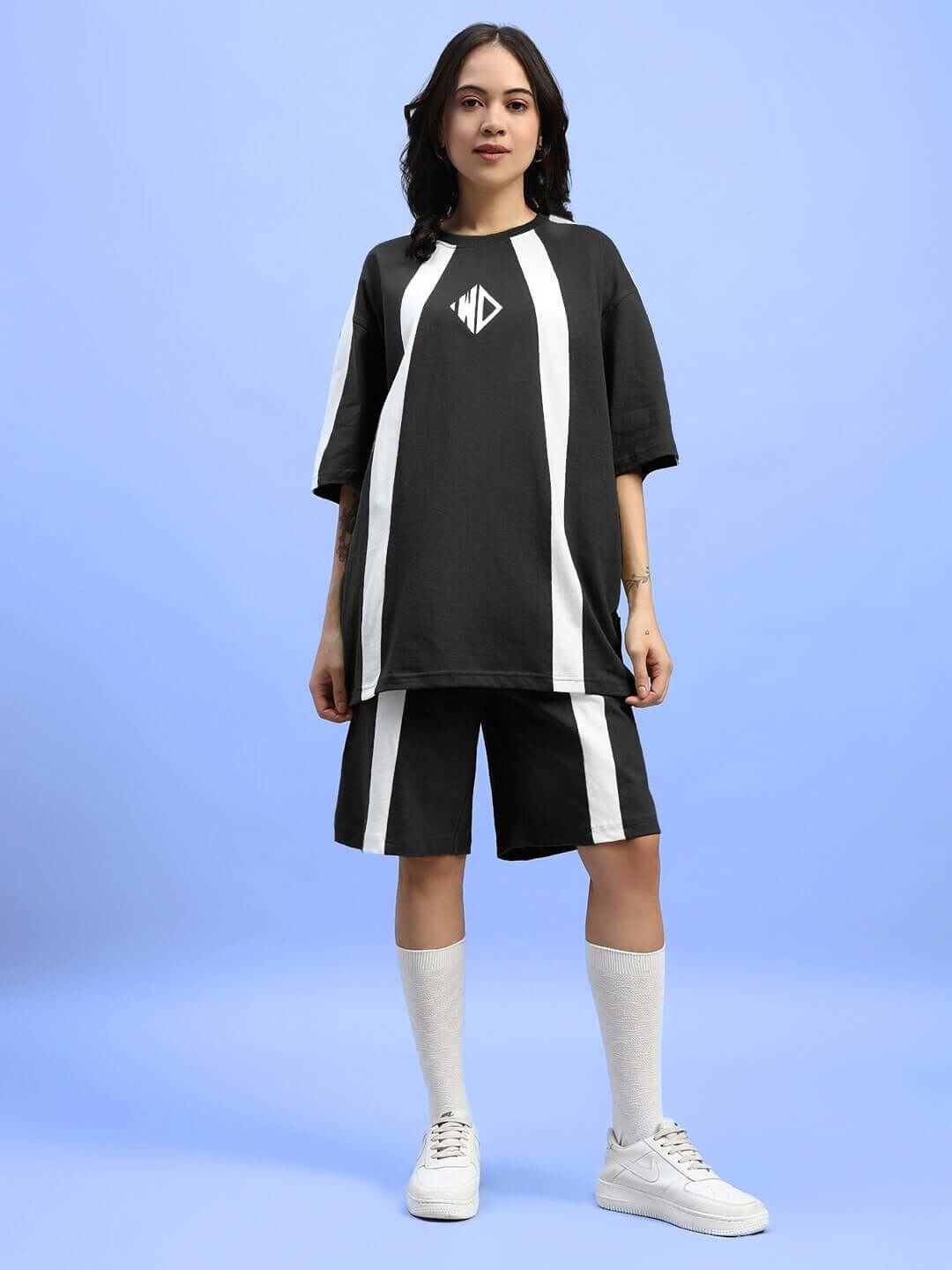 Woman wearing black wideline summer co-ord set with white stripes on a blue background.
