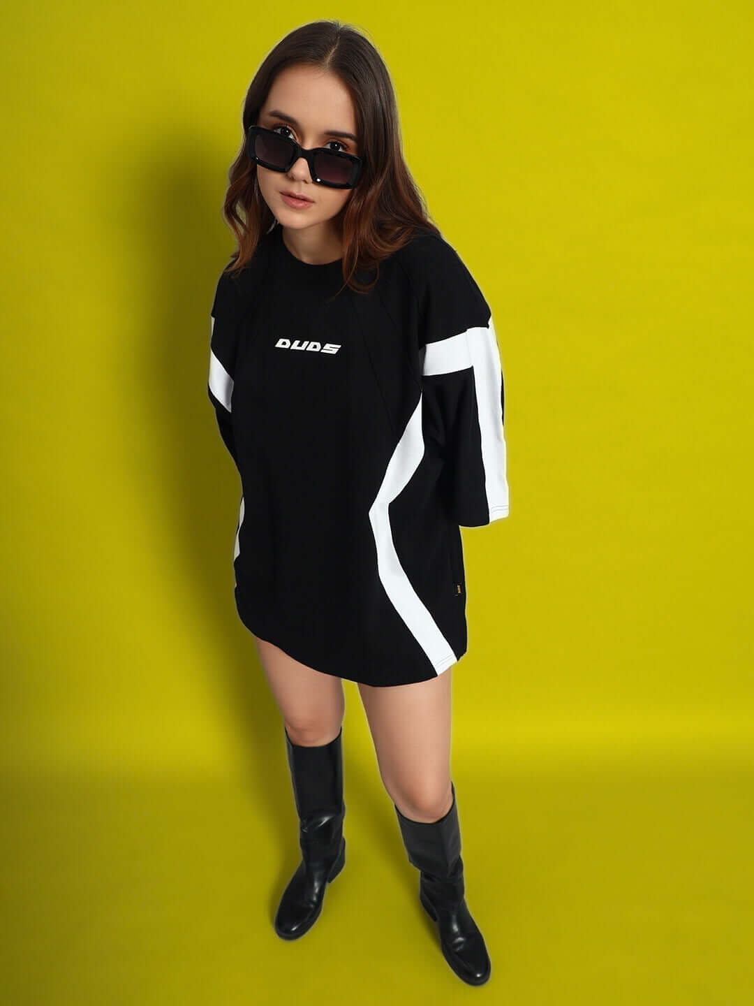 Model wearing Women's Wild Force Oversized T-Shirt in black-white with bold graphics, styled with sunglasses and boots on a bright background.