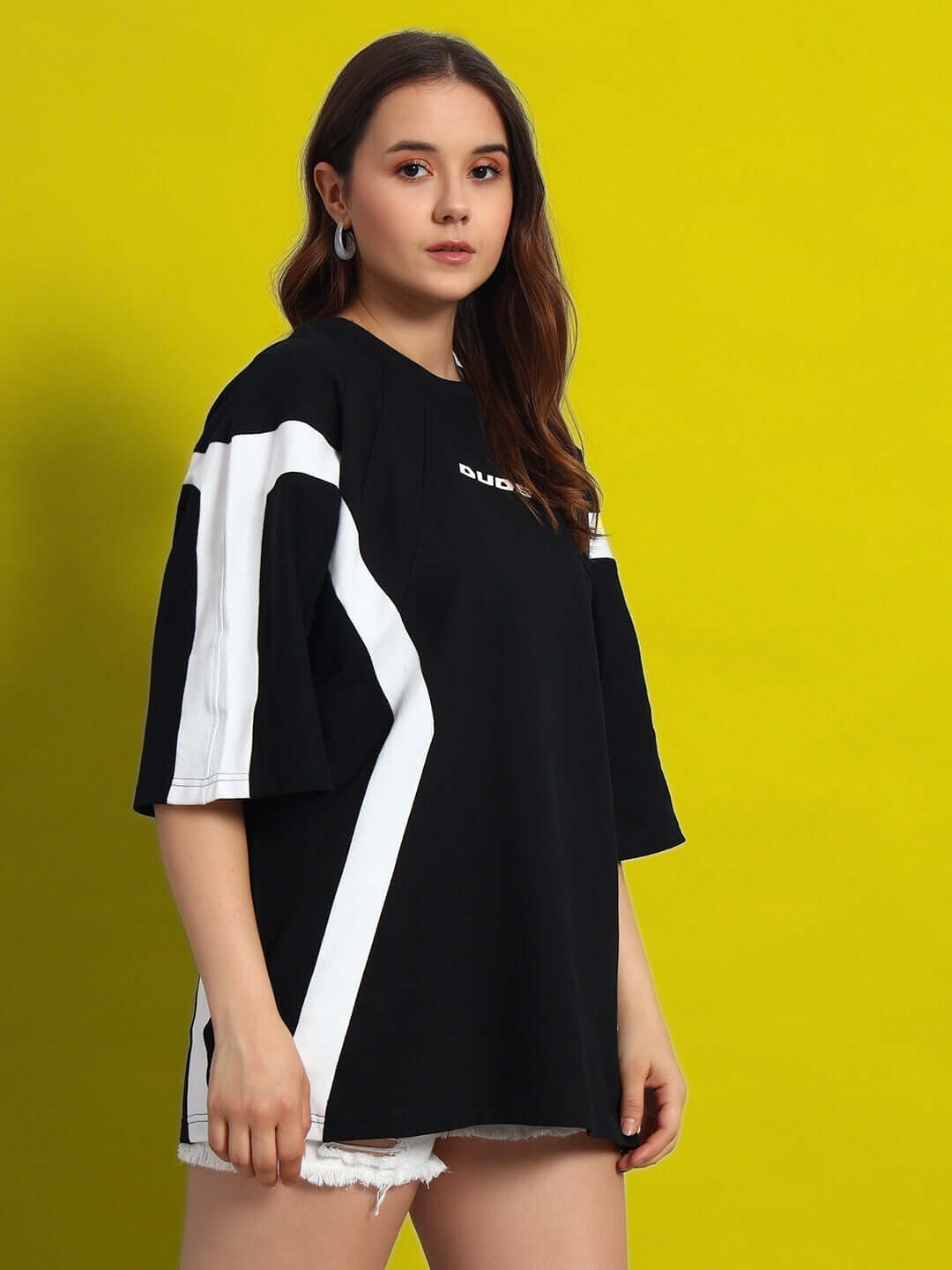 Women's oversized black and white T-shirt, premium cotton fabric, styled with white stripes, worn by model against yellow background.
