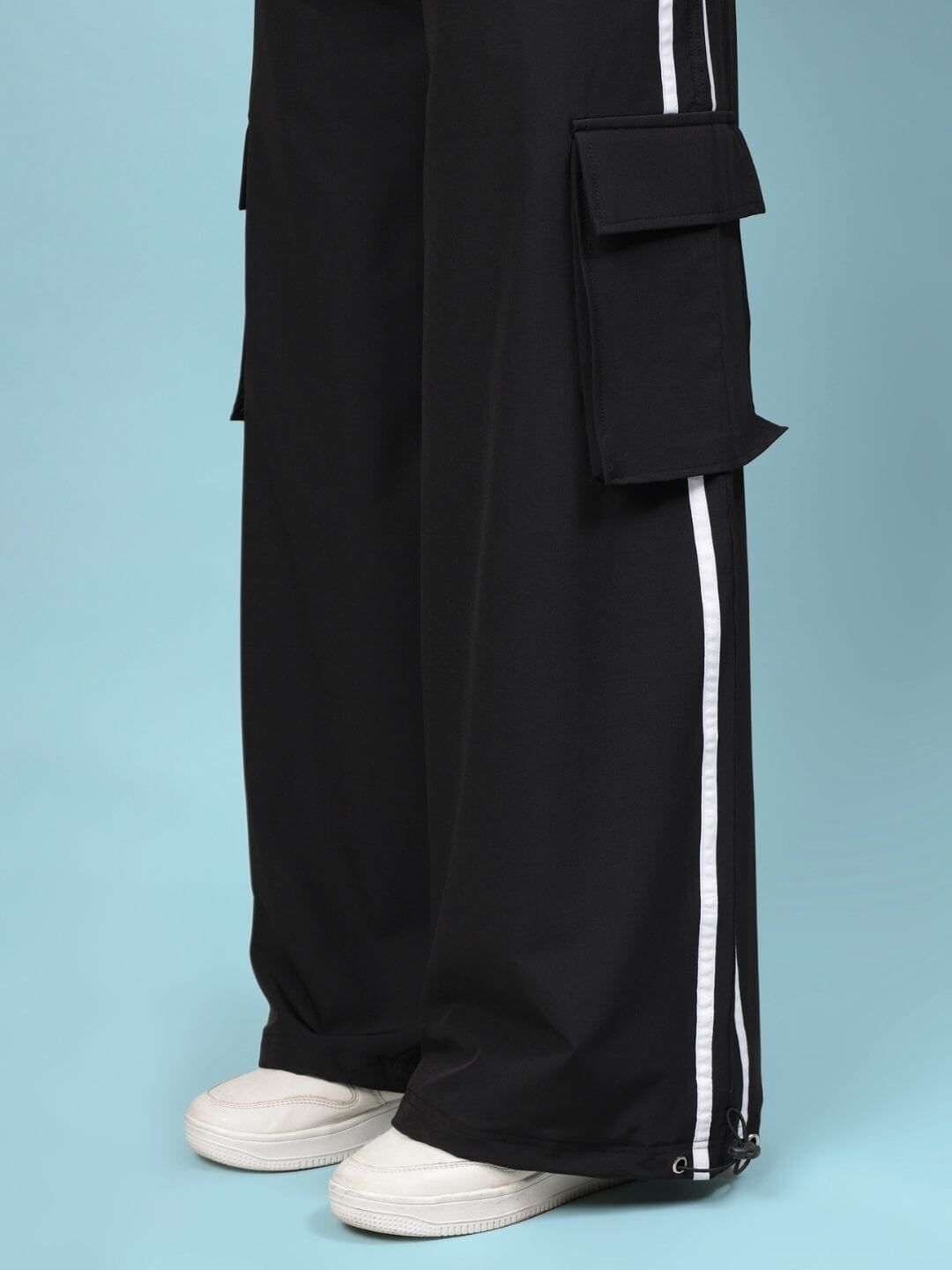 Model wearing WOMEN'S XAVIER CO-ORD SET BLACK with cargo pants and white sneakers against a blue background.