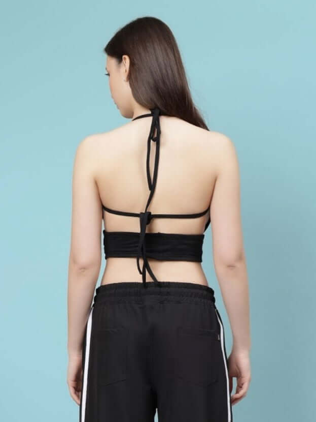 Woman wearing black Women's Xavier Criss Cross Crop-Top from the back, showing halter neck design with blue background.