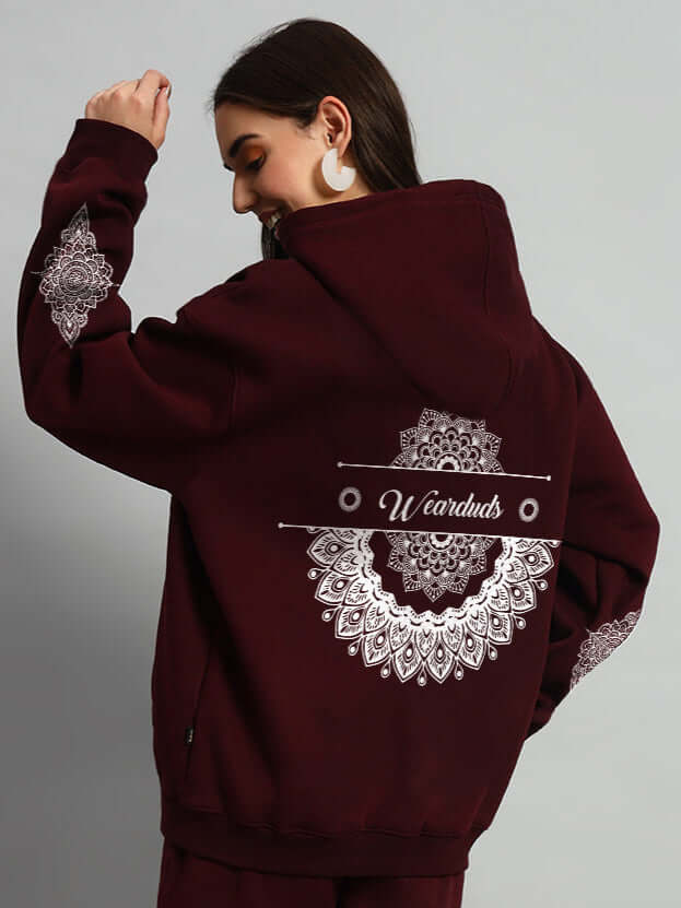 Woman wearing WOMENS YANTRA FLEECE HOODIE WINE with intricate mandala designs on sleeves and back, showcasing style and comfort.