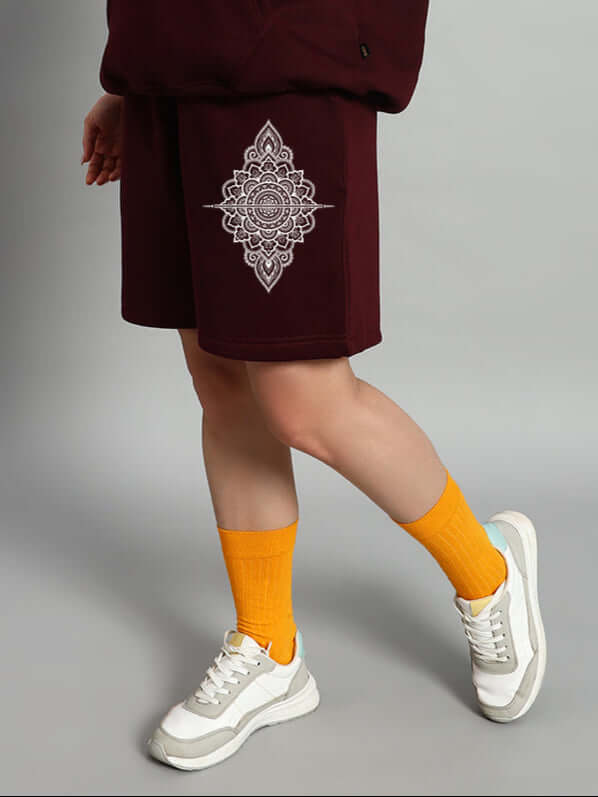 Person wearing WOMEN'S YANTRA FLEECE SHORTS WINE embroidered with mandala pattern, paired with yellow socks and white sneakers.