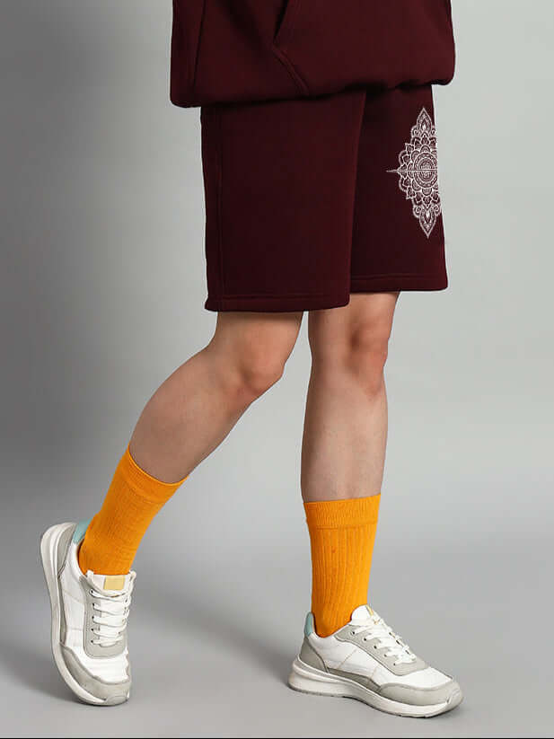 Model wearing WOMEN'S YANTRA FLEECE SHORTS WINE with white sneakers and yellow socks