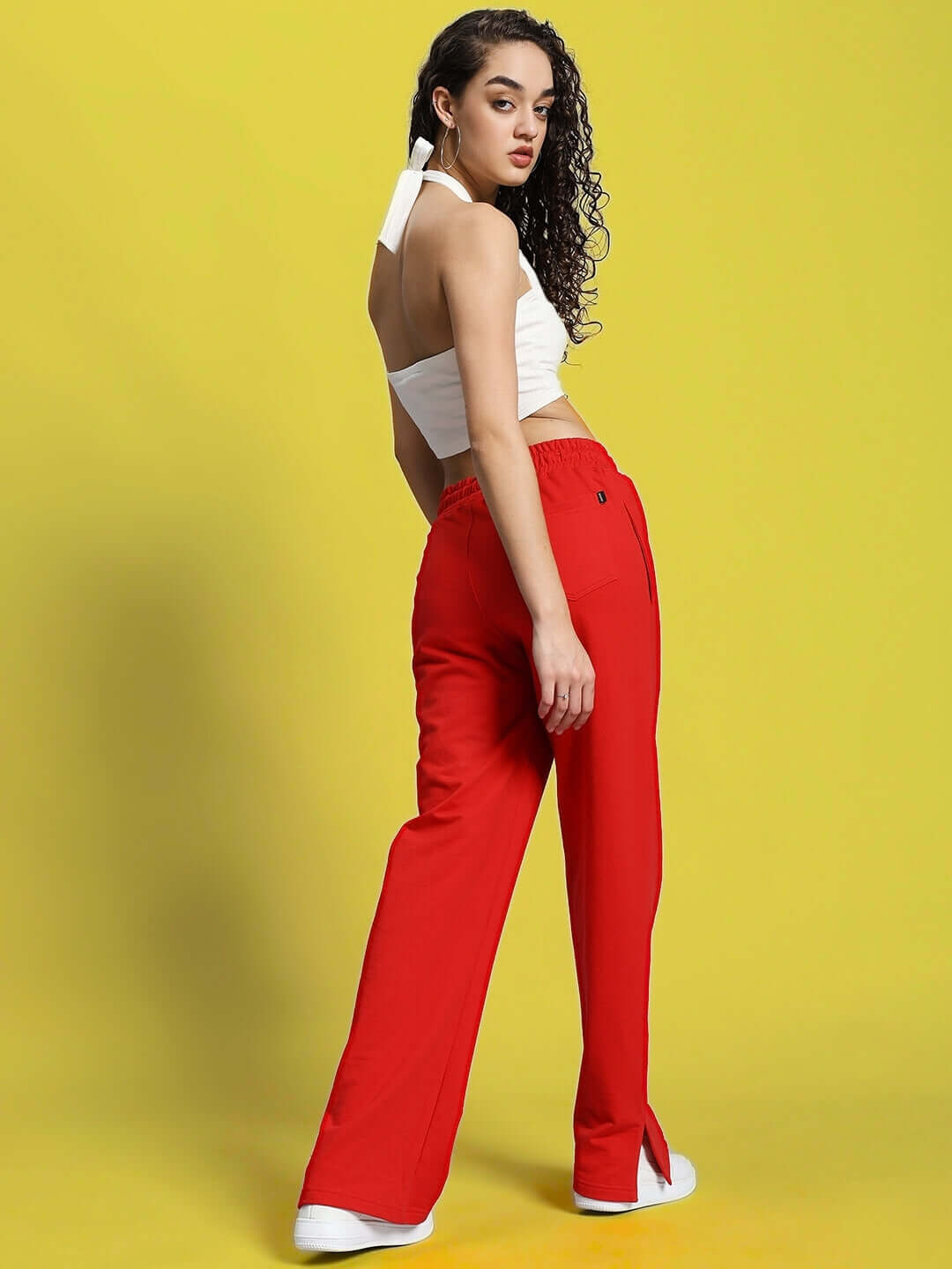 Woman wearing red women's Zion side slit joggers with a white top, standing against a bright yellow background.