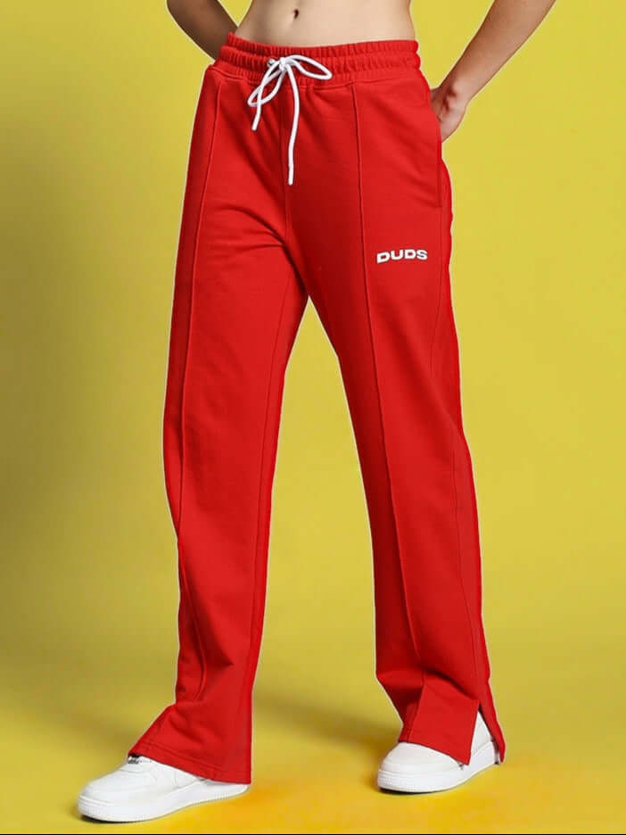 Women's red joggers with side slits by DUDS, featuring a comfortable fit and drawstring waist on a vibrant yellow background.