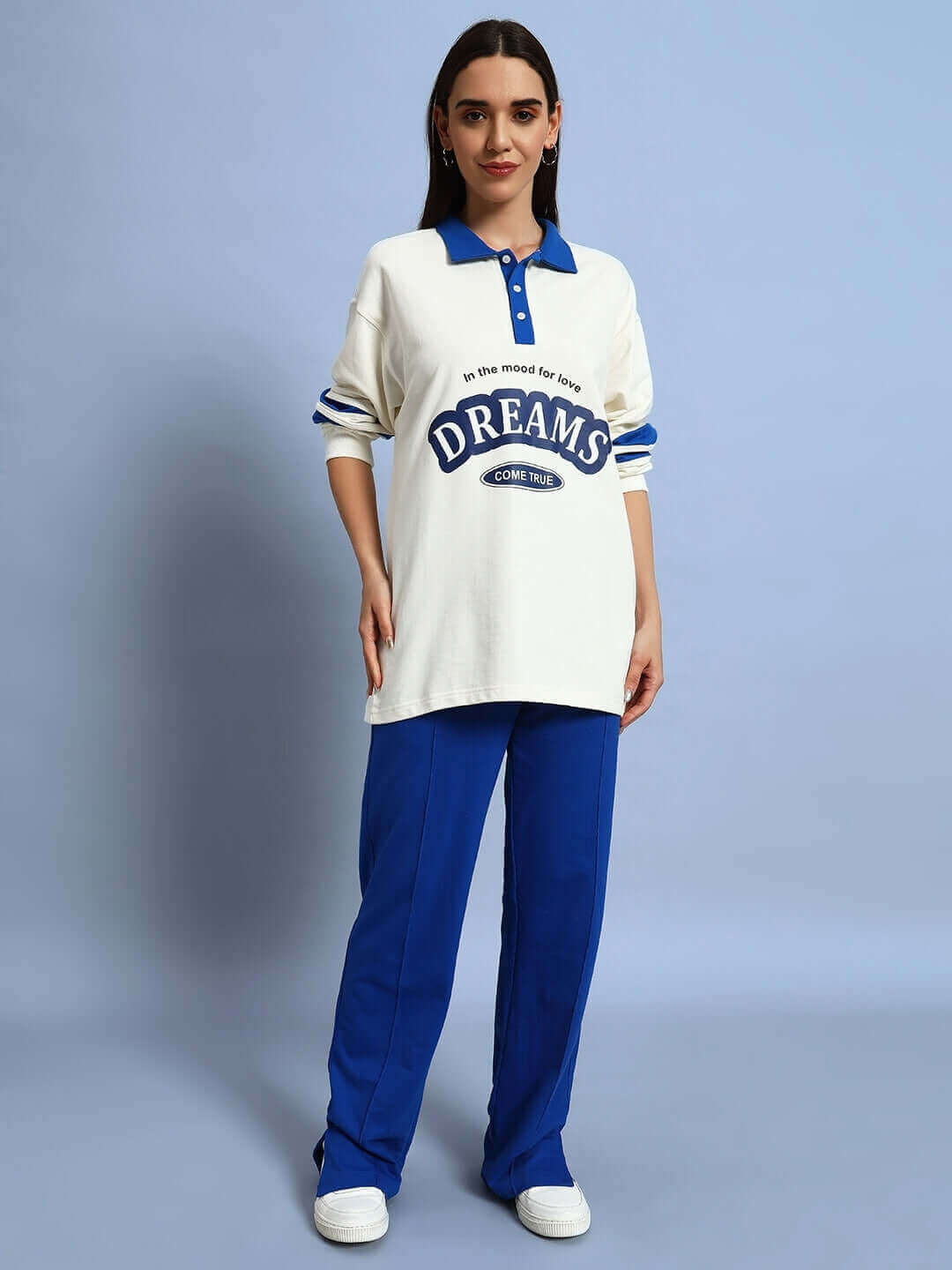 Woman wearing a white top with 'Dreams' text and royal blue joggers, standing against a light blue background.