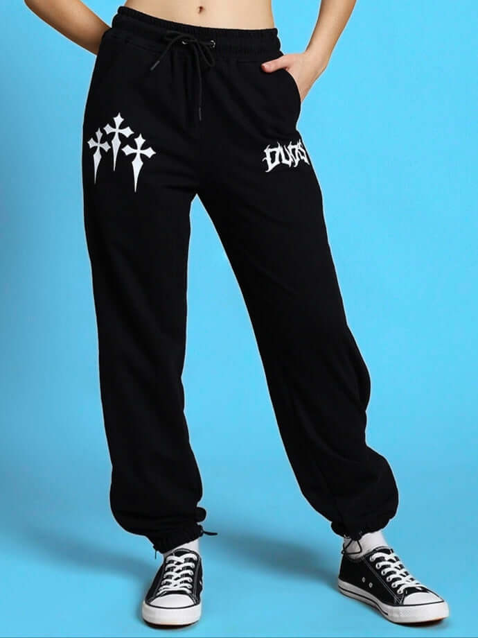 Black women's joggers with graphic details, styled with a drawstring waistband and paired with sneakers on a blue background.