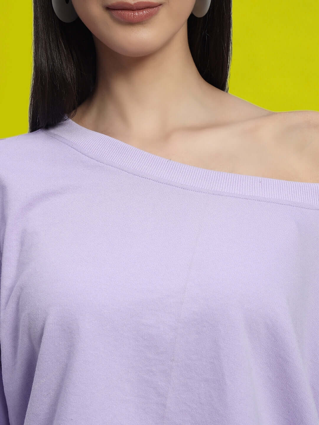 Close-up of a woman wearing a lilac off-shoulder top, showcasing premium fabric and relaxed fit, set against a vibrant yellow background.