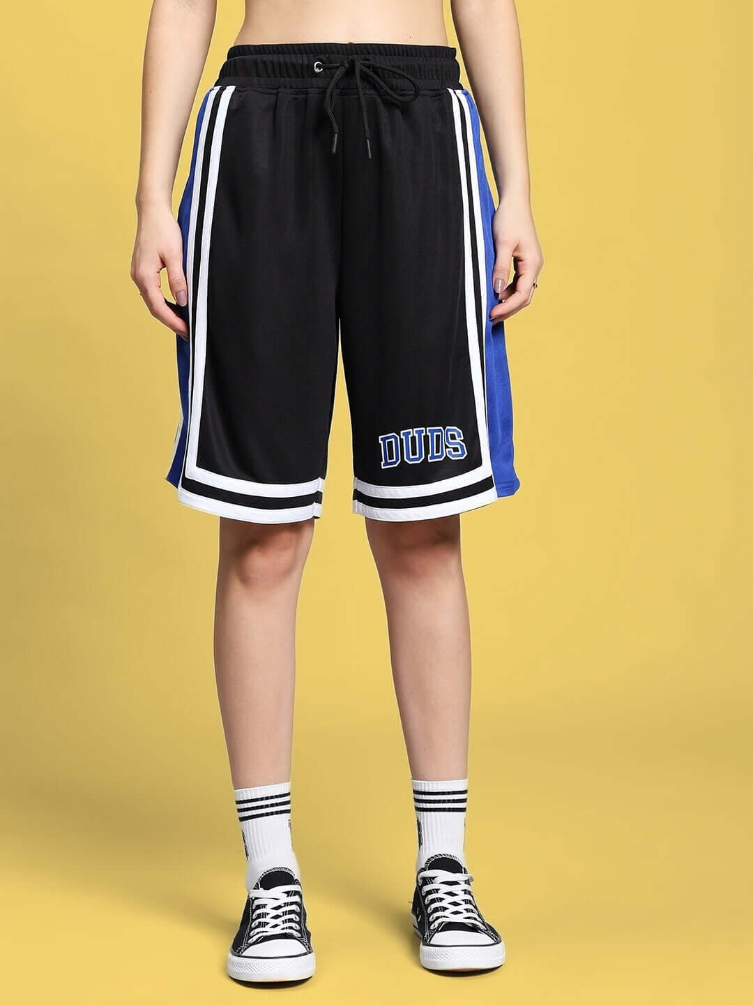 Model wearing black and blue 'DUBS' basketball shorts with stripes on yellow background