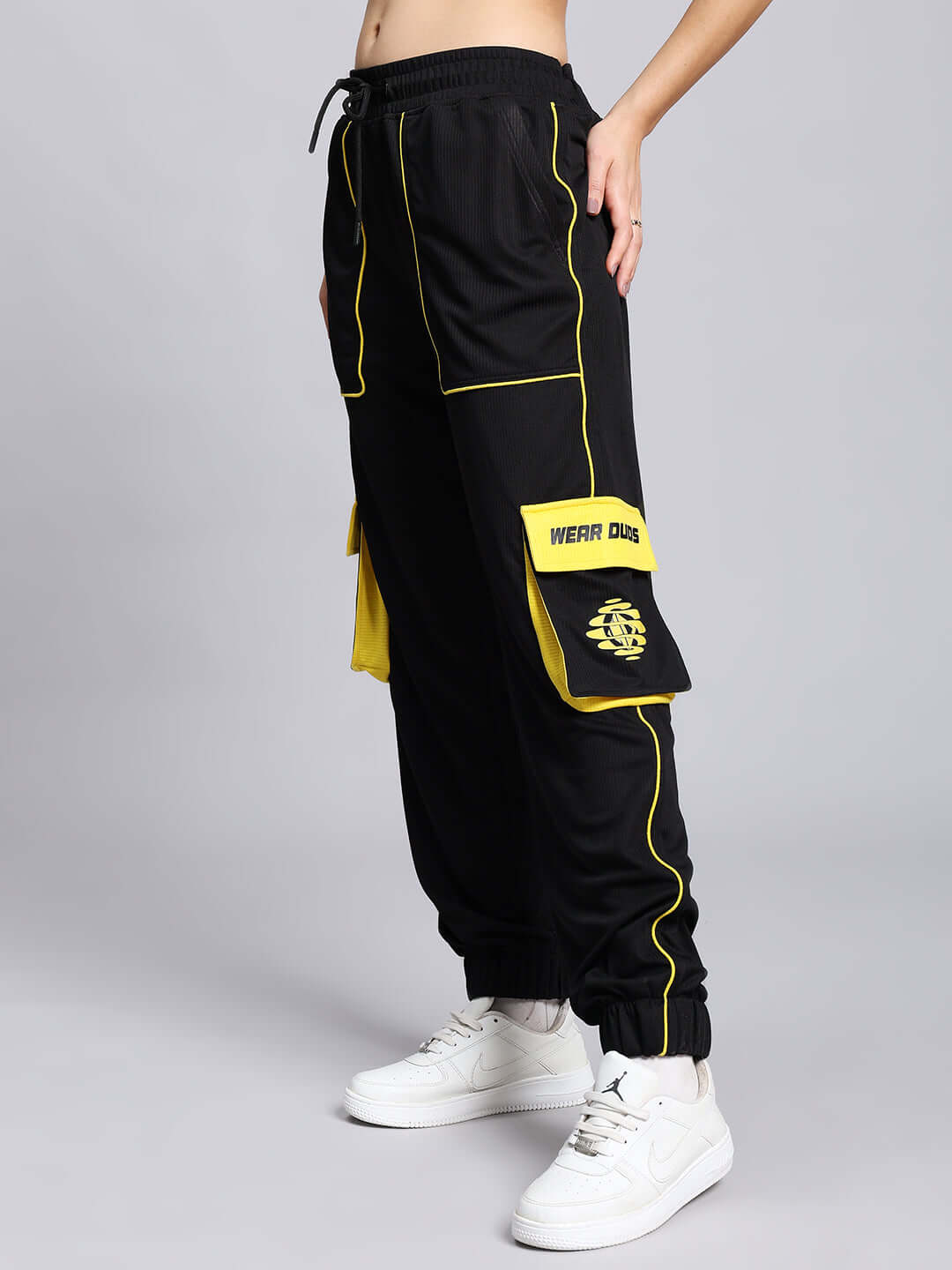 Black women's soccer cargo joggers with yellow detailing and pockets, worn with white sneakers.