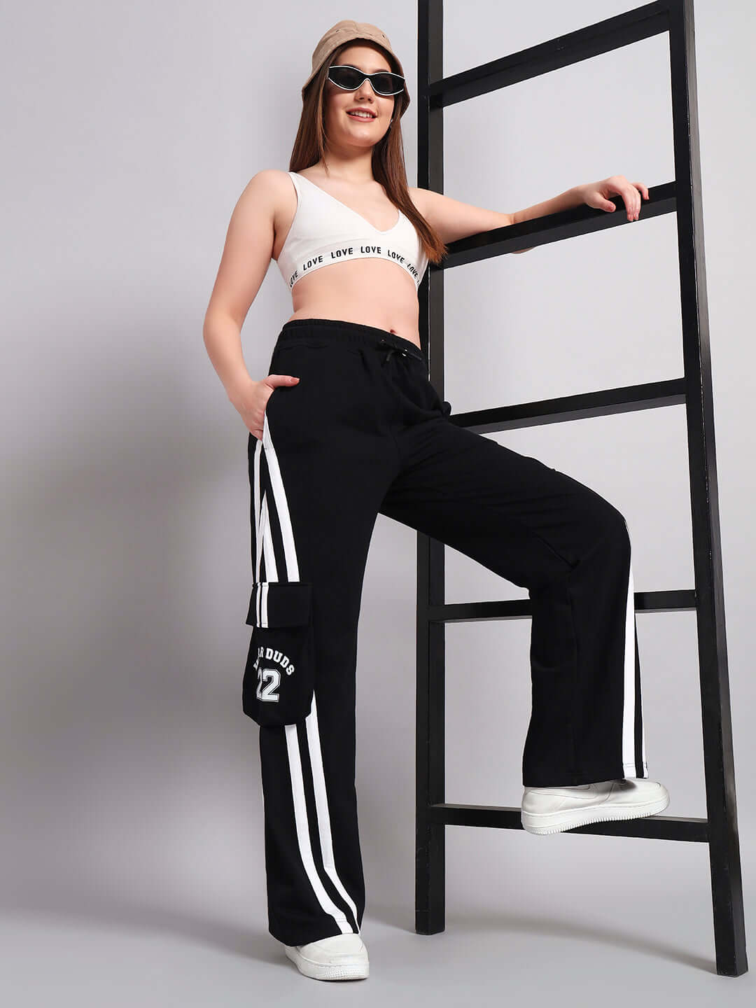 Woman wearing WOMENS CRUCIS MULTI POCKET RELAXED-FIT JOGGERS BLACK with white stripe detail, leaning on a ladder for a modern, sporty look.