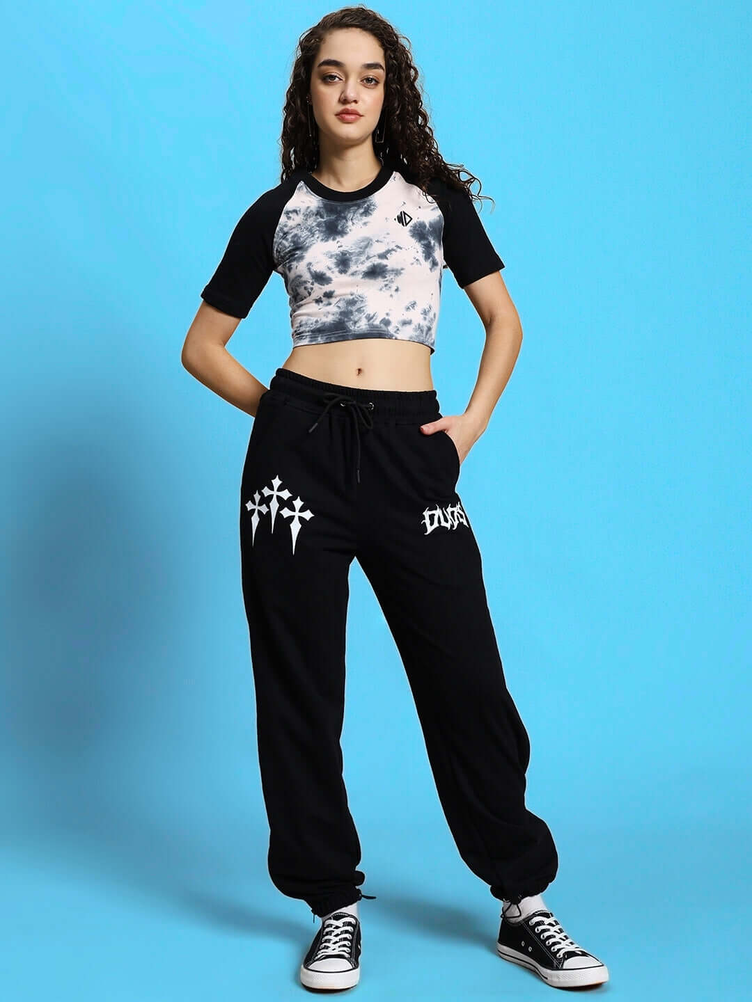 Casual black and white co-ord set with patterned top and black joggers, worn by a model standing against a bright blue background.