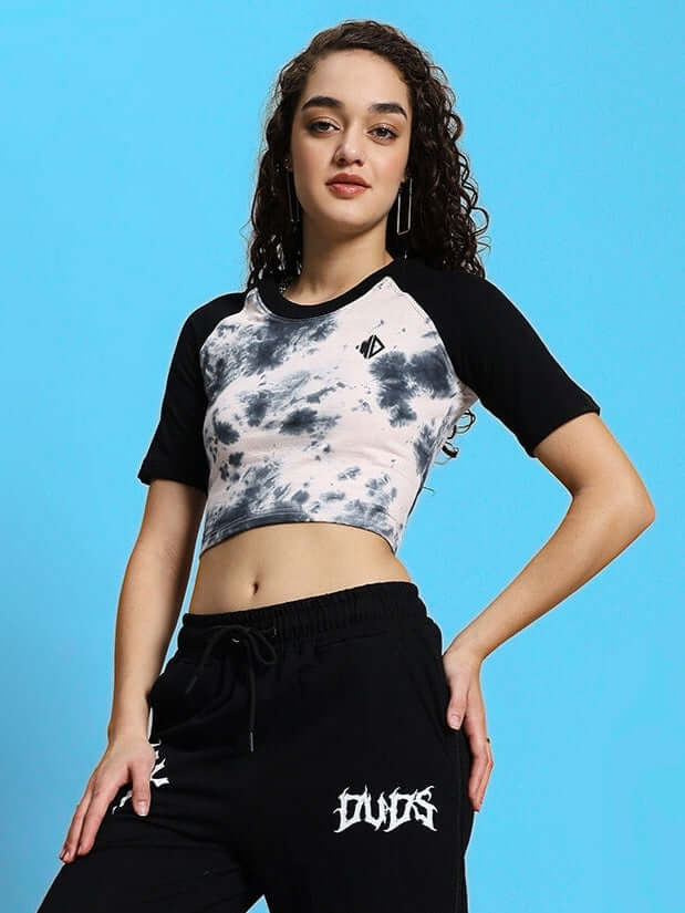 Model wearing a black-beige Cantik crop-top, 100% cotton, bio-washed, styled with casual pants against a blue background.