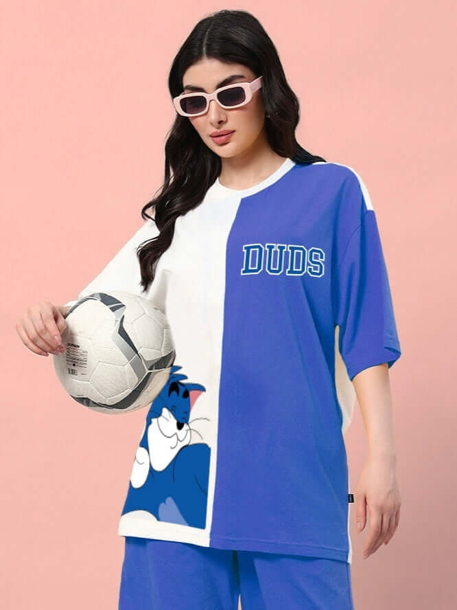 Woman wearing a blue and white oversized t-shirt with cartoon print, holding a soccer ball, stylishly paired with sunglasses.