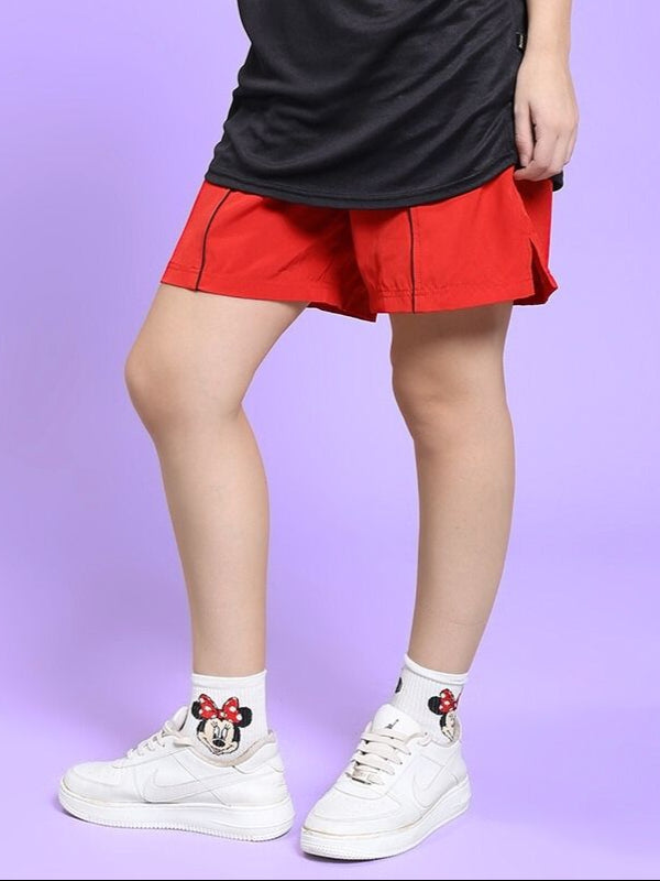 Model wearing WOMEN'S CHAMPION ZONE FRONT PLATED SHORTS RED with white sneakers and character socks, standing in profile.