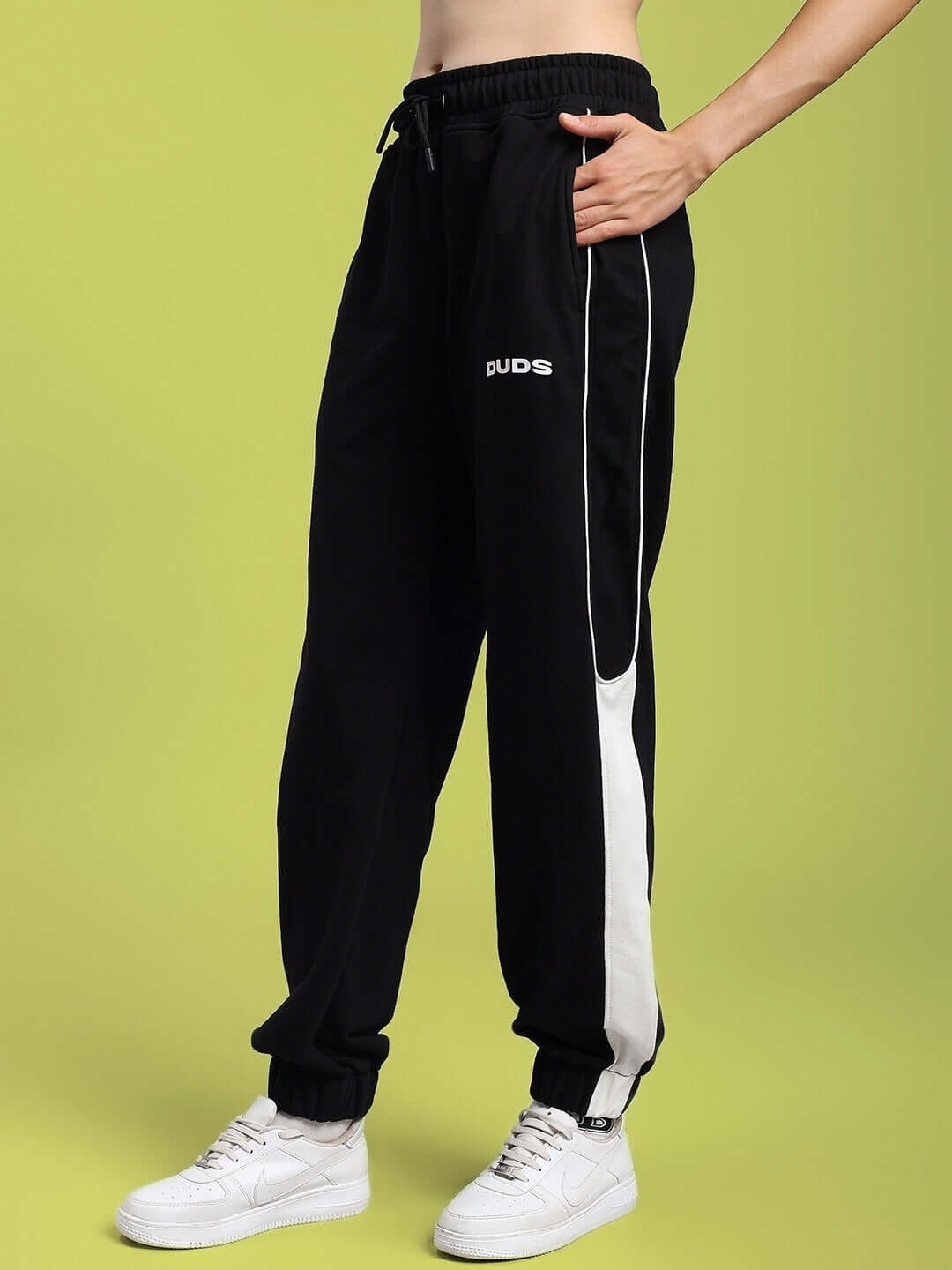 Woman wearing black relaxed fit joggers with white stripe and DUDS logo, showcasing casual style and comfort.