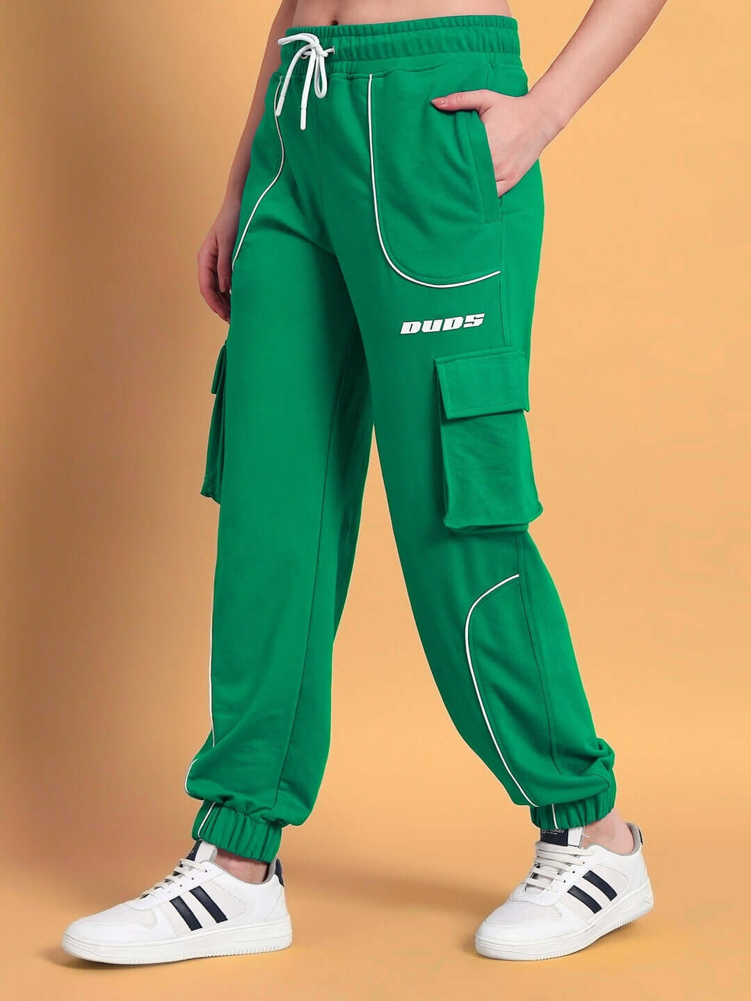Model wearing green women's relaxed-fit joggers with pockets, featuring white stitching detail and logo print. Stylish casual wear.