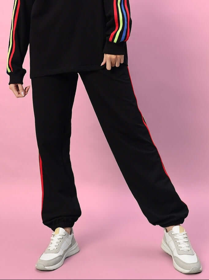 Women's DUDS black joggers with rainbow colorful stripes, made to order for a custom fit, shown against a pink background.