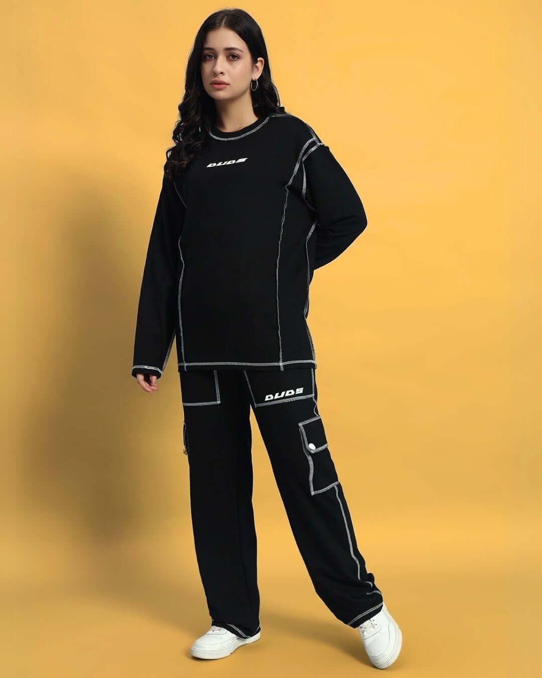 Woman wearing black WOMEN'S DYNAMIC 5 POCKET CARGO PANT by DUDS, standing against yellow background.