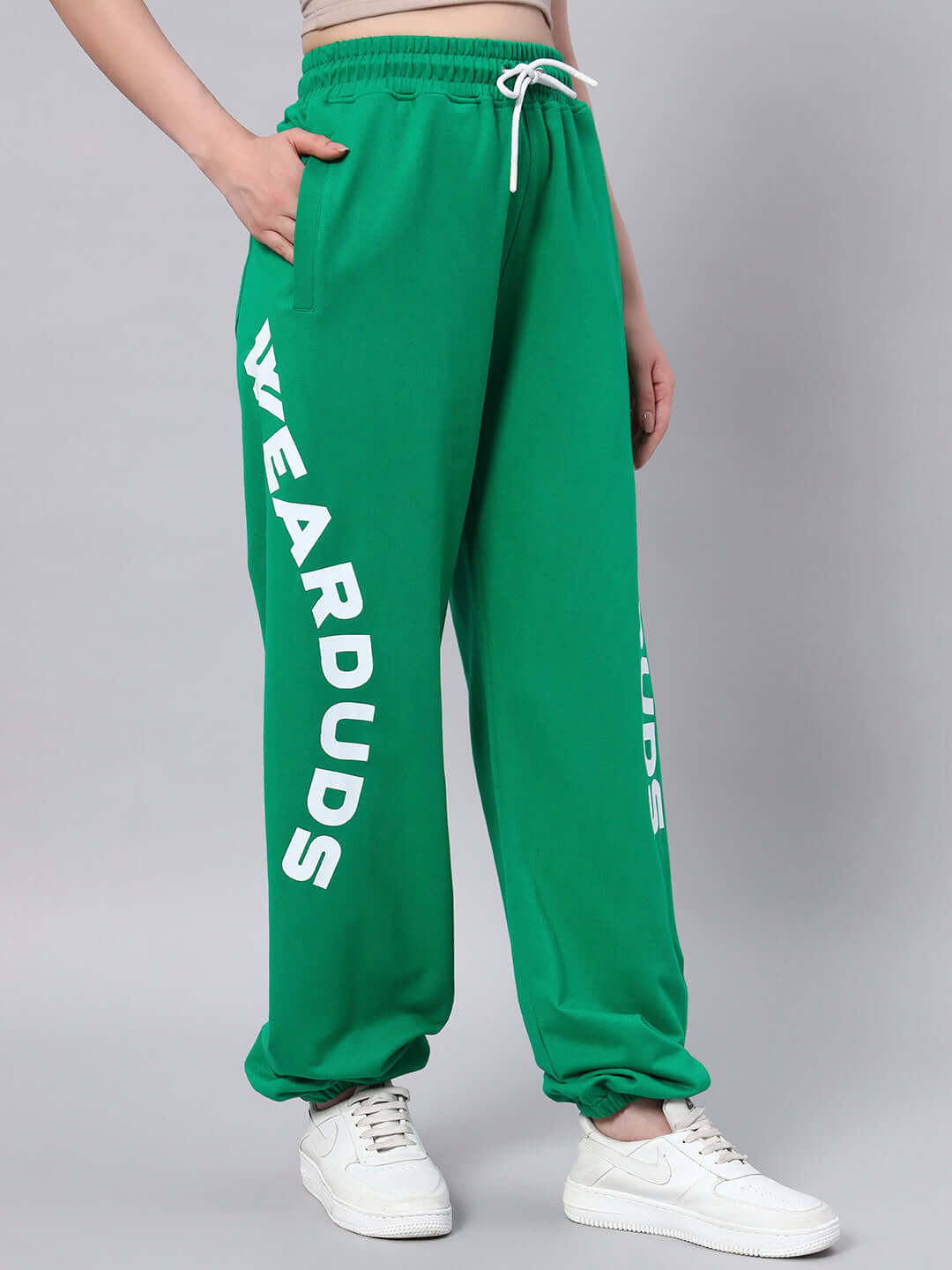 Woman wearing WOMEN'S ELLEN RELAXED FIT JOGGER GREEN with white sneakers, featuring 'WEARDUDS' print on the leg.