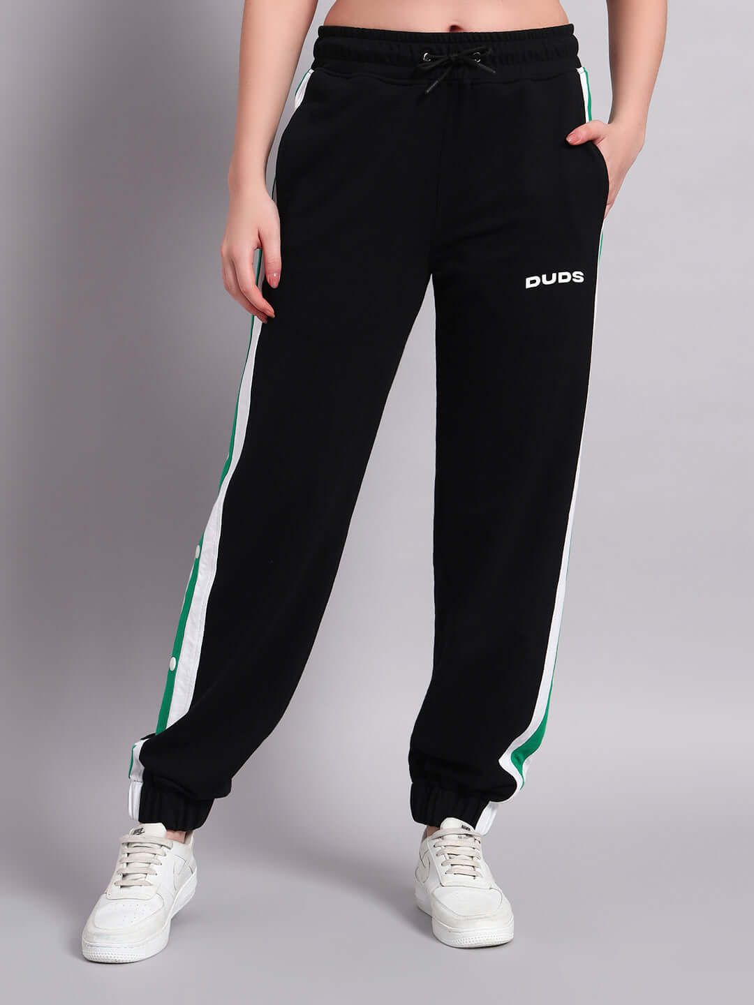 Woman wearing black joggers with green and white Emirati stripes from DUDS, hands in pockets.