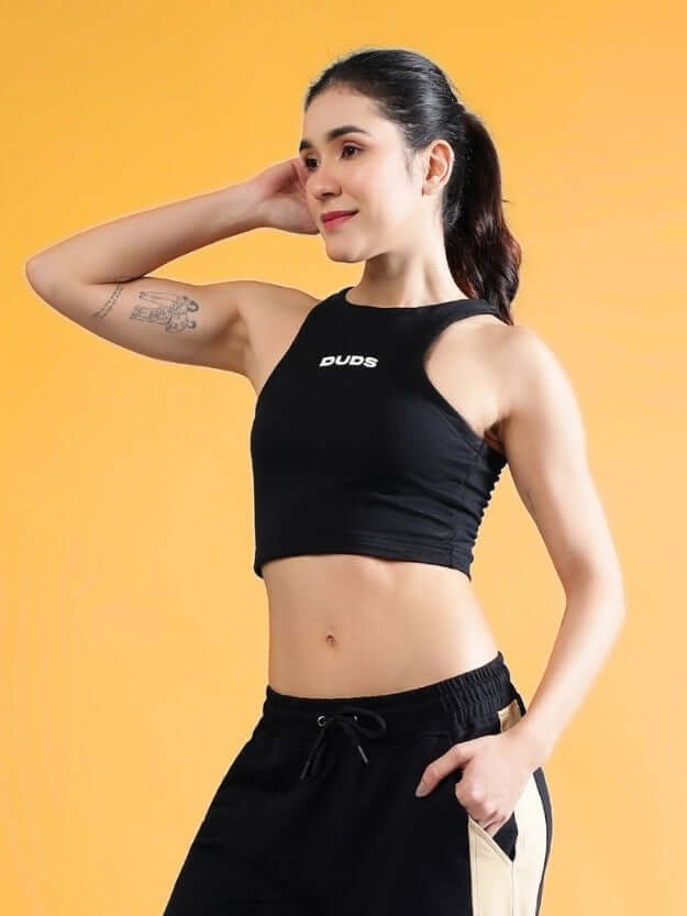 Woman wearing a black crop top and sporty pants, posing confidently against an orange background, showcasing fitness attire.