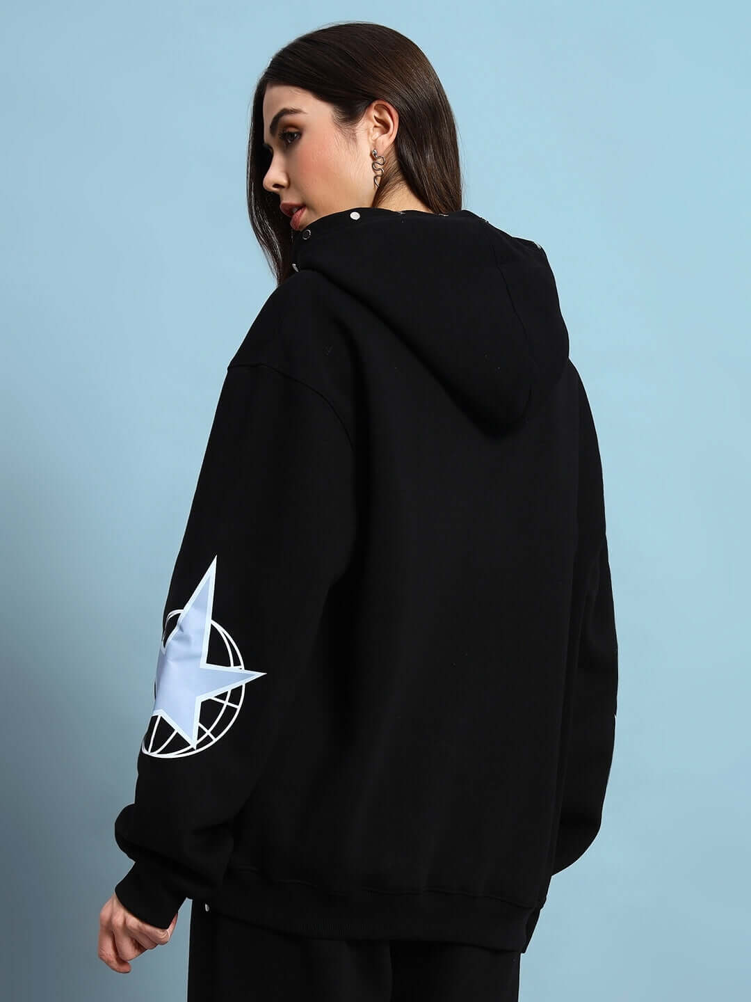 Woman wearing WOMEN GLOBAL FLEECE HOODIE BLACK with star design on sleeve, showcasing streetwear style and comfort.