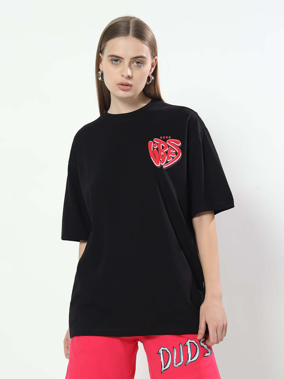 Model wearing Women's Good Vibes oversized black T-shirt with red logo, paired with vibrant pink shorts by DUDS.