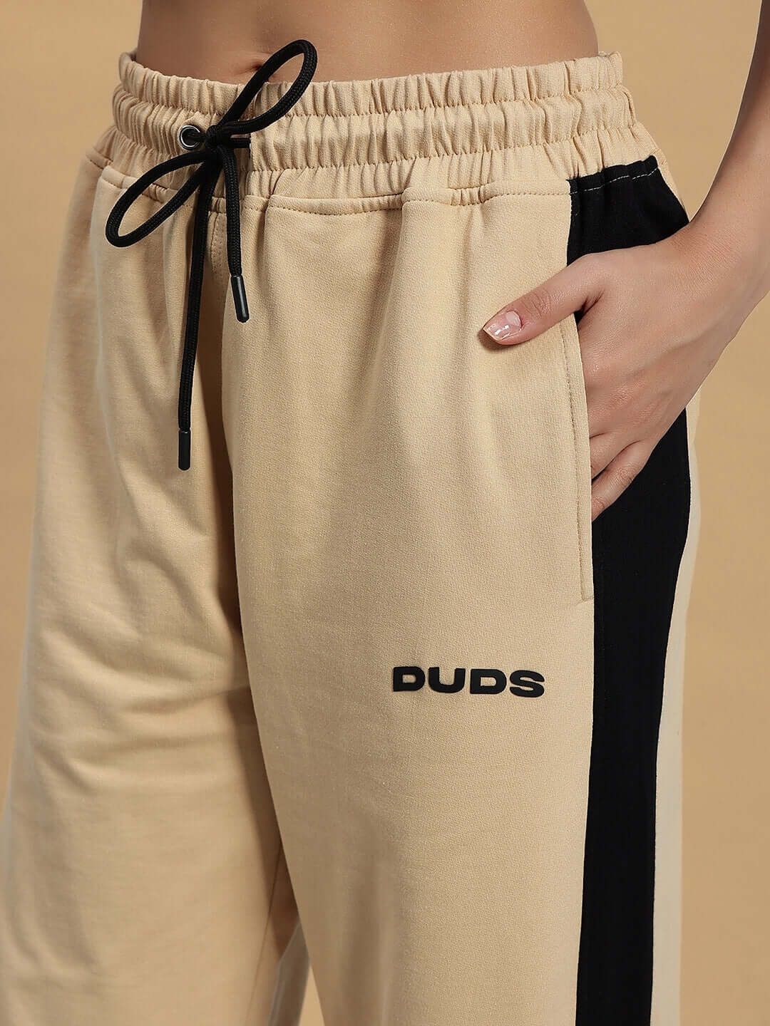 Close-up of women's beige-black DUDS baggy joggers with drawstring, emphasizing comfortable fit and stylish design for customizable wear.