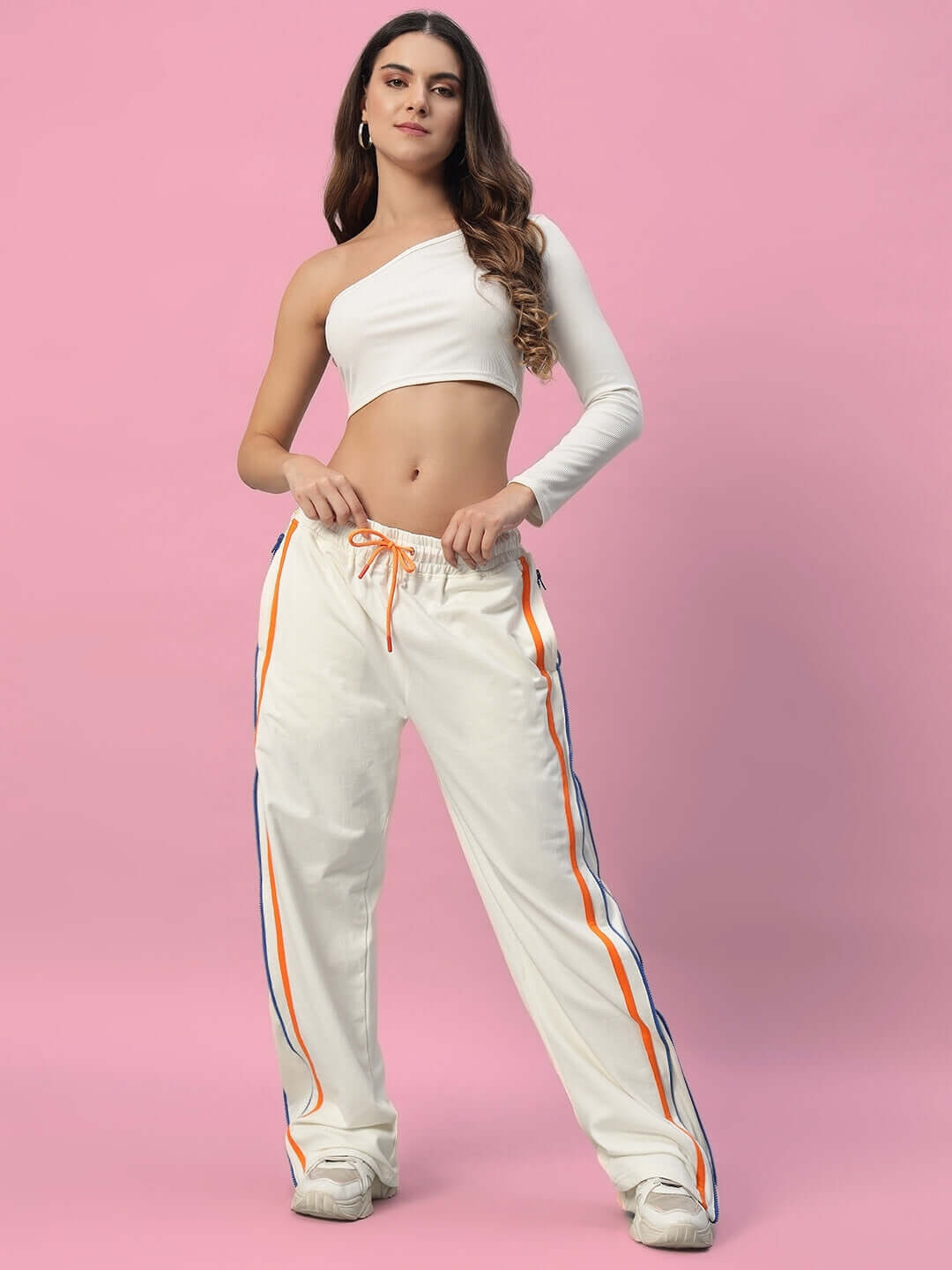 Alt Tag: Model wearing Women's Imperial Side Zipper Joggers in off white with colorful side stripes, posed against a pink background.