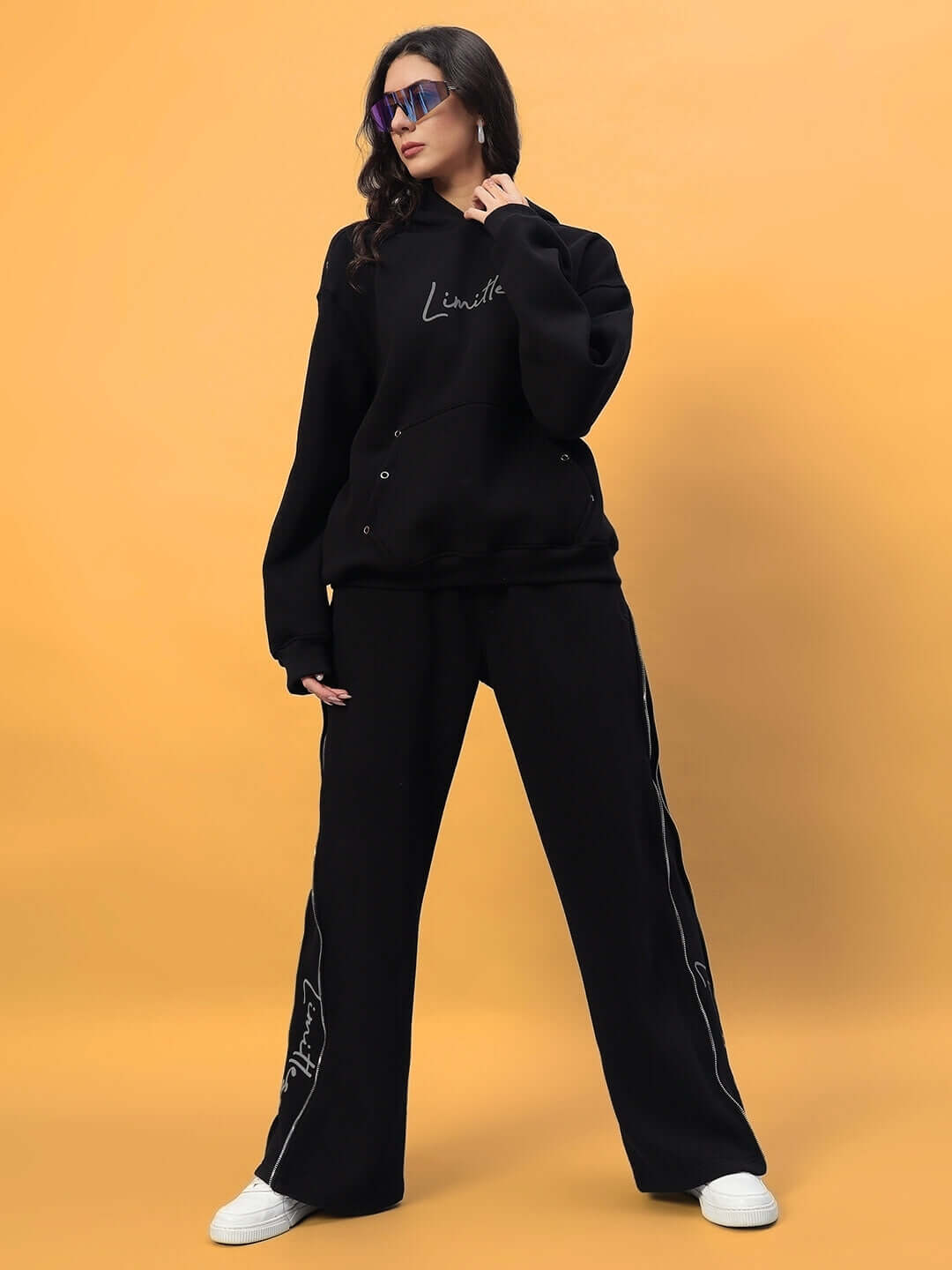 Woman wearing Women's Limitless Fleece Reflector Jogger in black, styled with matching top and white sneakers, on a yellow background.