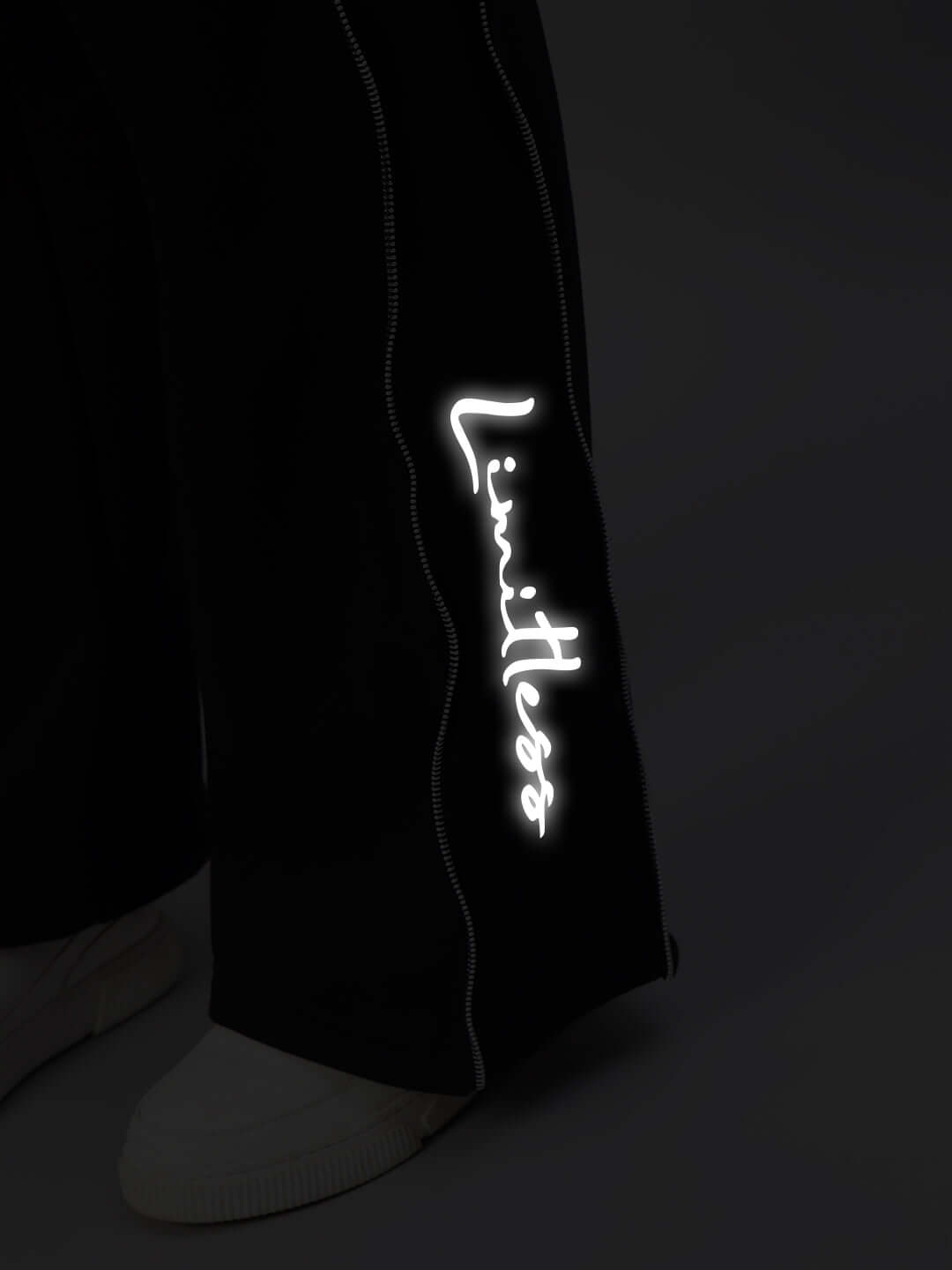 Close-up of Women's Limitless Fleece Reflector Jogger in Black, showcasing reflective 'Limitless' text and white stitching detail.