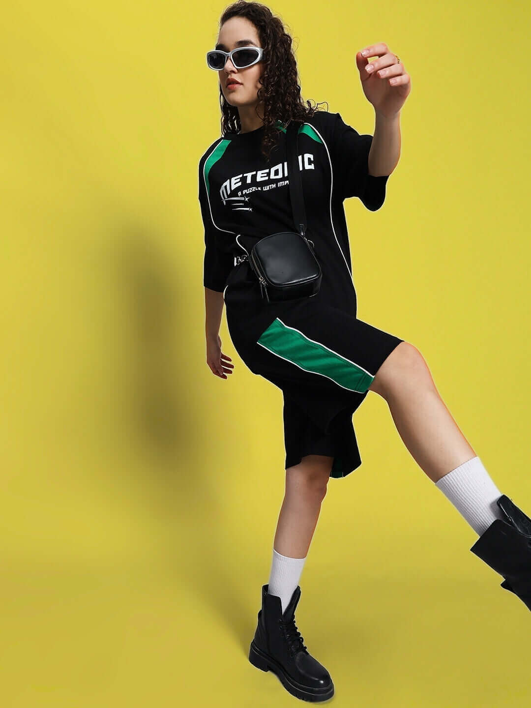 Model wearing Women's Meteoric Regular Fit Shorts in black against yellow background, showcasing sporty style with boots and sunglasses.