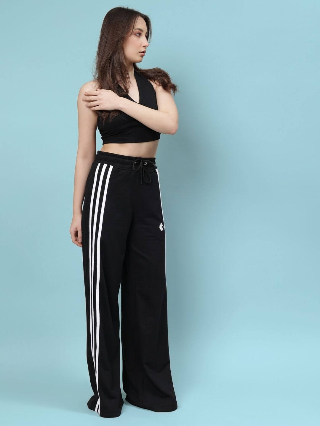 Woman wearing a black crop-top paired with black wide-leg pants featuring white stripes on a blue background.