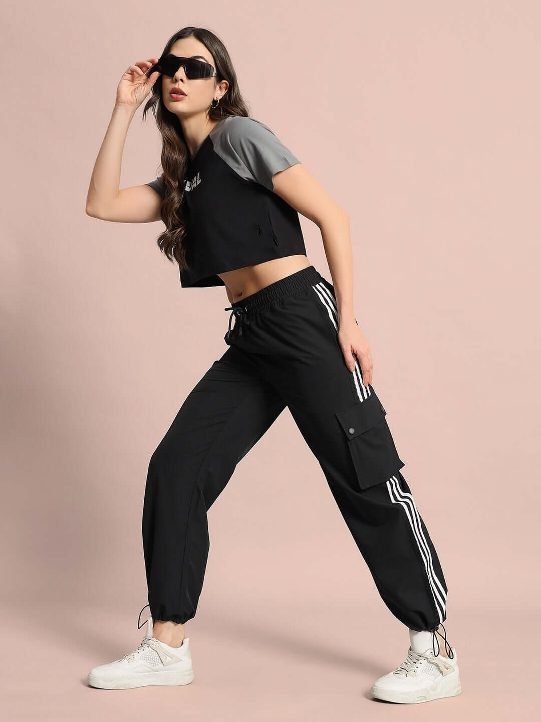 Woman wearing black Nova relaxed fit cargo pants with white stripes and pocket detailing, styled with a sporty top and sunglasses.