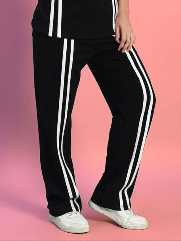 Women's black jogger with two white stripes, crafted by DUDS tailors, showcased on a pink background.