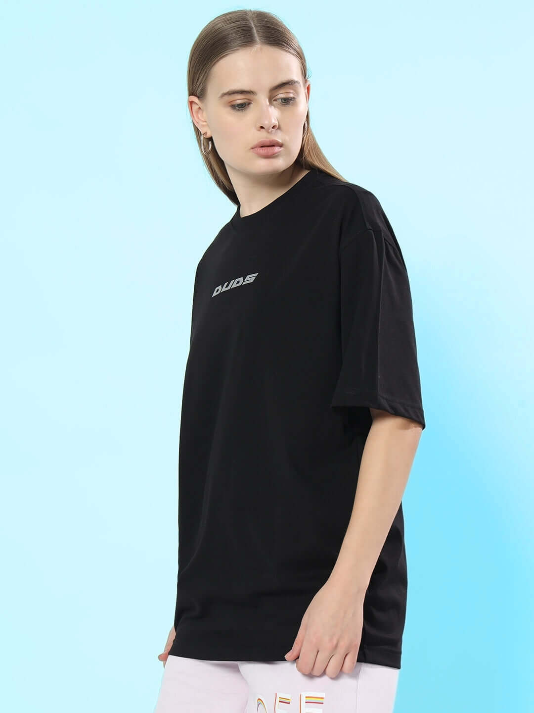 Woman wearing a black oversized T-shirt made of premium cotton, styled with a minimalist design, against a blue background.