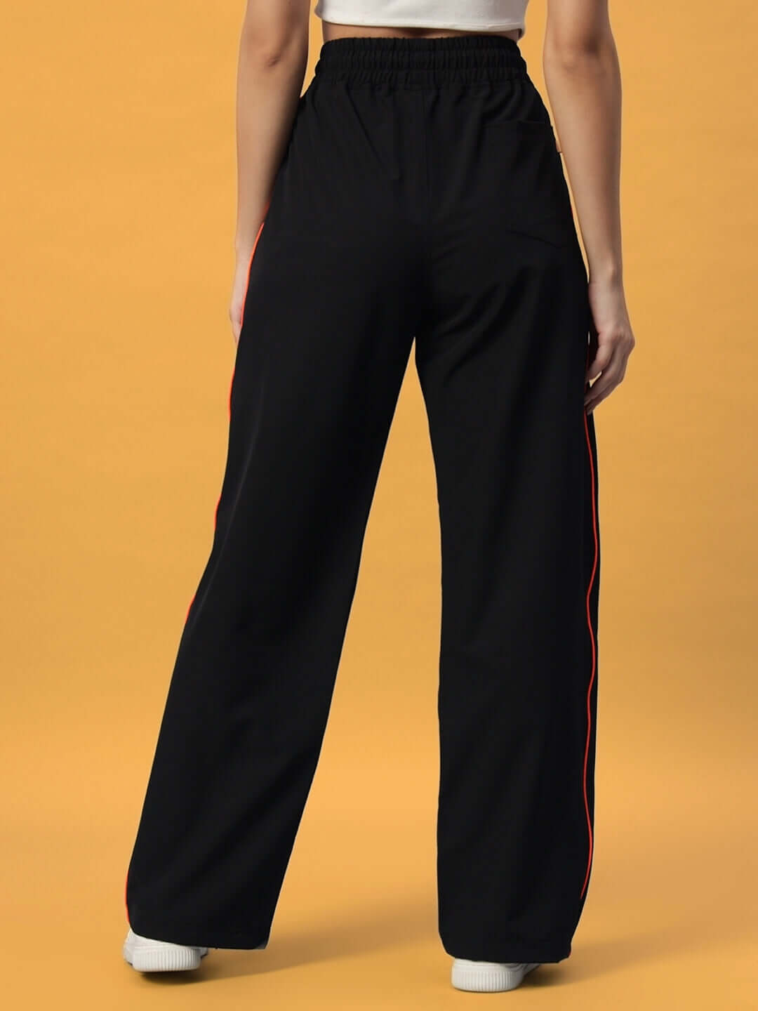 Back view of women's black Raider Relaxed Pant Jogger with red side trim, worn by a model against a yellow background.